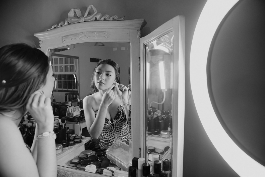 São os detalhes que fazem a diferença. Os últimos retoques e a colocação dos brincos em frente à penteadeira, em um registro elegante em preto e branco.