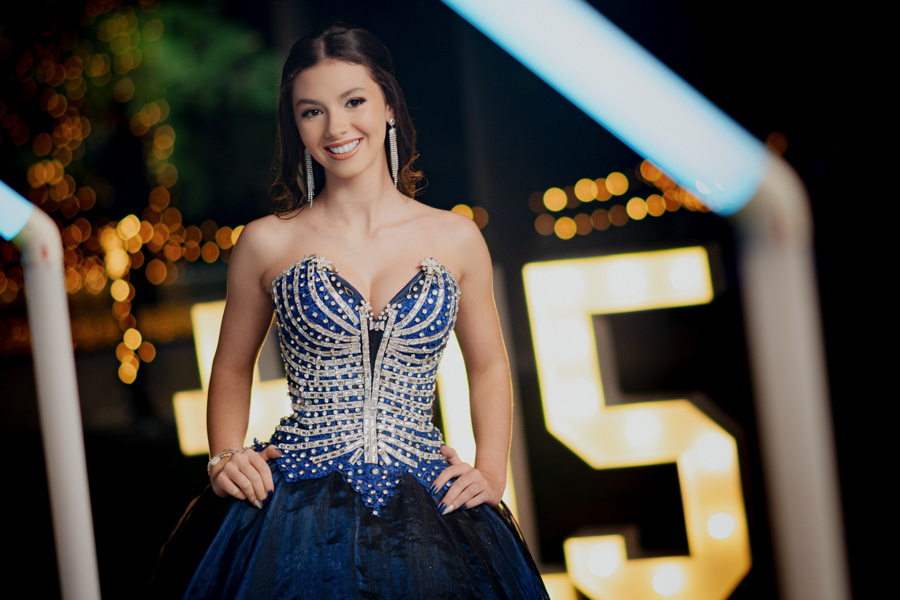 um belo sorriso foto de meio corpo, Pronta para brilhar! A debutante deslumbrante em seu vestido de gala azul, posando em frente ao letreiro iluminado #15 na decoração incrível do Buffet Dona Lucy.