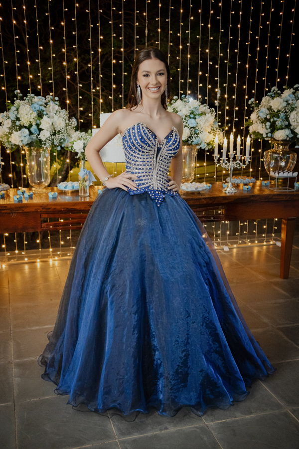 Brilho e sofisticação em cada detalhe. A debutante posa com seu vestido azul deslumbrante, cercada pela decoração iluminada e encantadora do Buffet Dona Lucy em Jacareí.