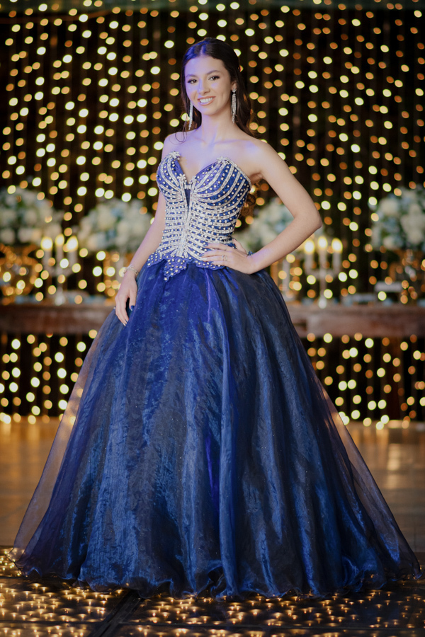 Pose de princesa! Com as mãos na cintura, a debutante exibe a elegância do seu vestido bordado em frente à mesa de doces impecável no Buffet Dona Lucy.