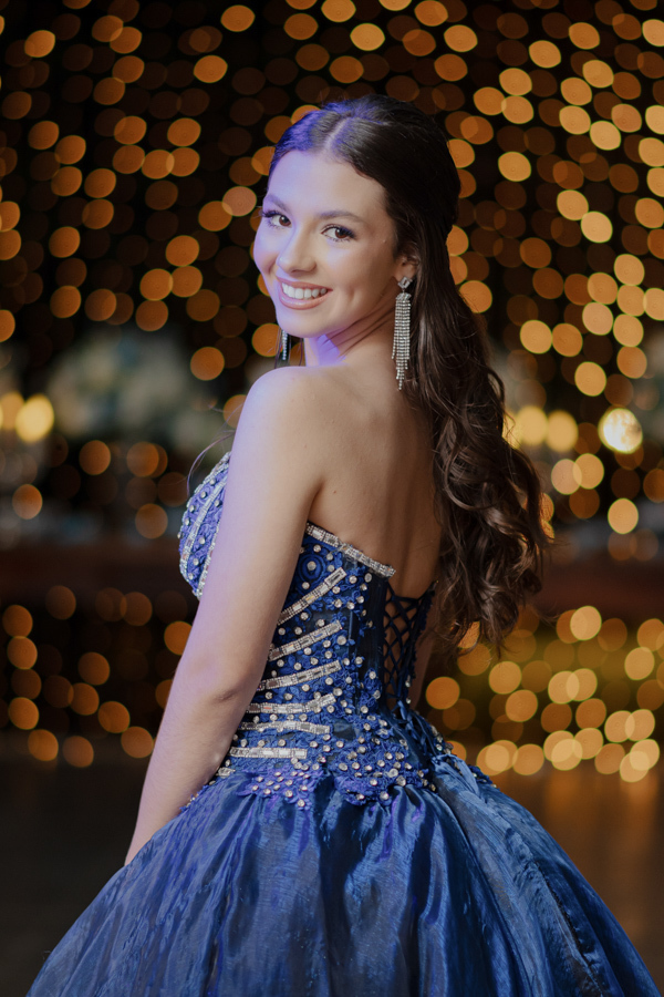 Um olhar radiante sobre o ombro. Close na beleza da aniversariante, realçando o penteado, os brincos e o brilho do vestido nesta noite especial de 15 anos.