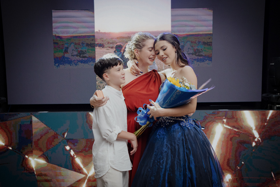 A entrega da joia. O momento simbólico em que o irmão coloca o anel de 15 anos na debutante, sob o olhar orgulhoso da mãe, marcando a transição para uma nova fase. eles se abraçam 