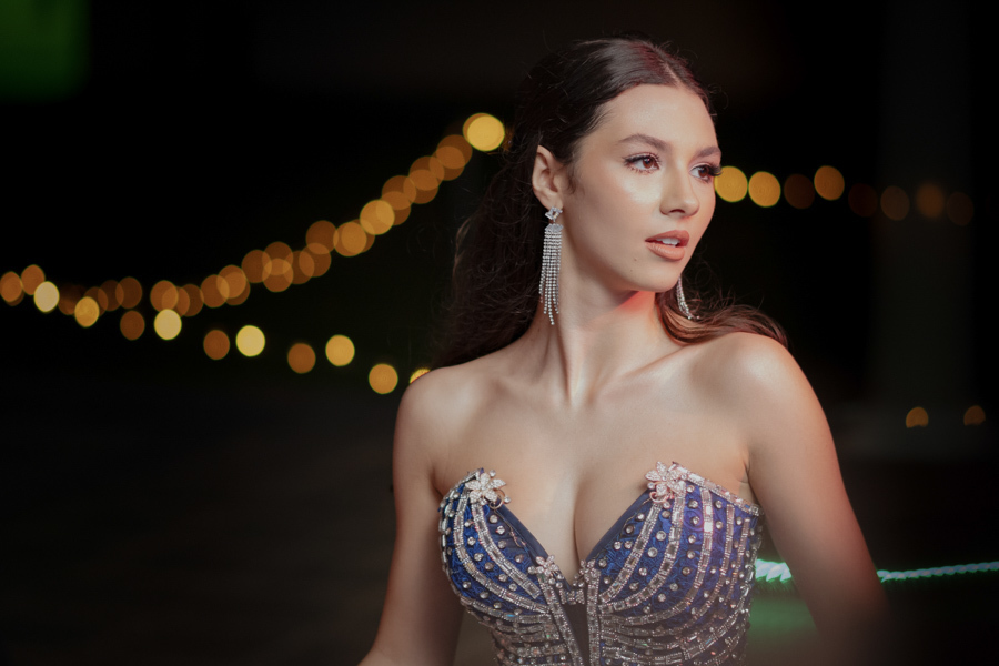 Detalhes de um sonho azul. Close no vestido de 15 anos, destacando o corpete bordado com pedrarias e a saia volumosa, com o fundo iluminado criando um bokeh mágico.