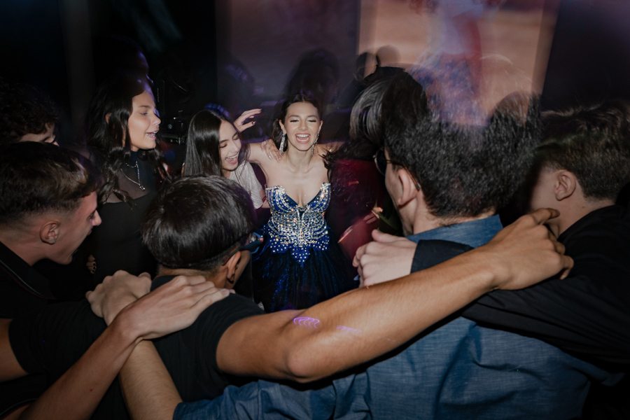 A energia lá em cima! A debutante e seus amigos pulam e se abraçam na pista de dança, celebrando a amizade e a alegria contagiante desta festa de 15 anos