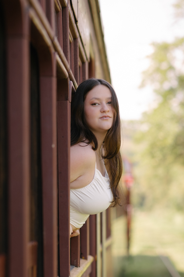 Olhar de esperança: Kiara na janela do trem Maria Fumaça. Retrato colorido destacando a beleza da debutante em Guararema - SP.