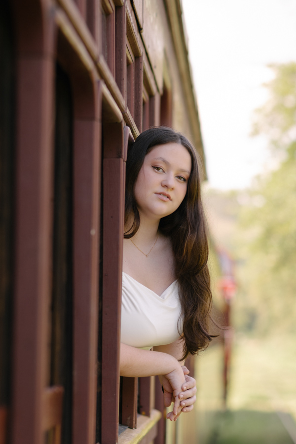 Charme ferroviário: Debutante posando na janela do trem histórico. As cores quentes da madeira contrastando com a leveza da Kiara.