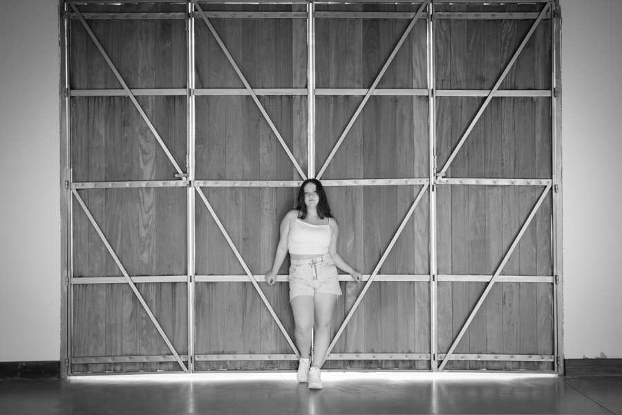 Grandiosidade e textura: Foto preto e branco em frente às grandes portas do galpão da estação. Arquitetura industrial no book de 15 anos.