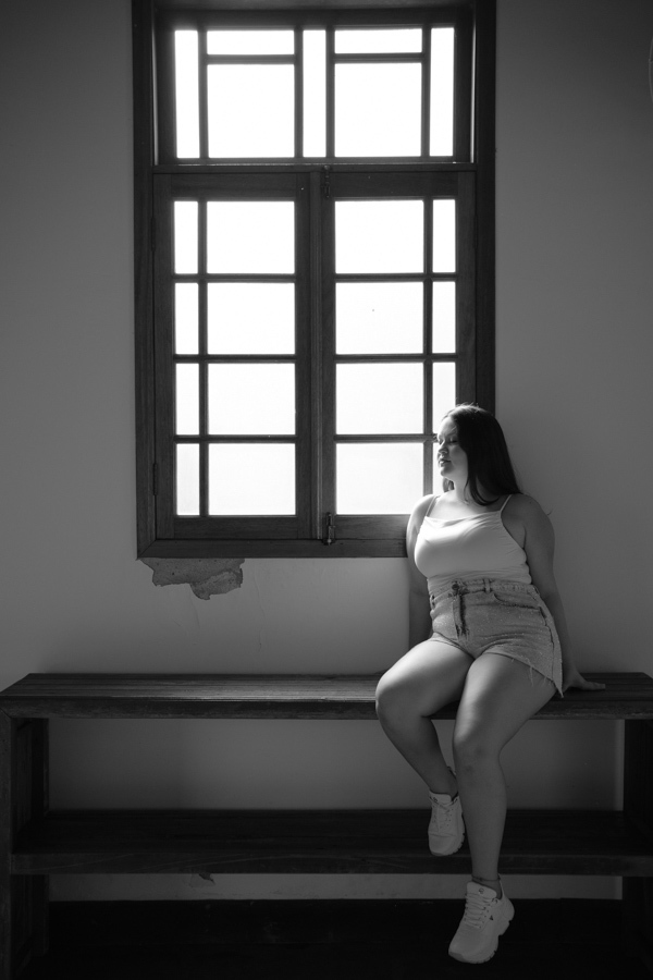 Luz dramática: Silhueta sentada na janela da estação. Fotografia P&B com alto contraste e emoção.