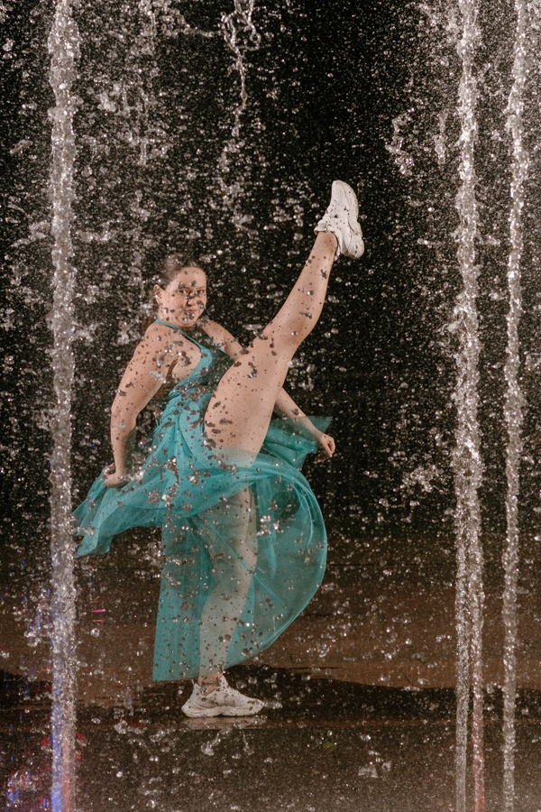 O Grand Finale: Energia e movimento! Kiara celebra seus 15 anos com uma pose impactante na fonte iluminada de Guararema. Fotografia noturna criativa congelando cada gota de água.