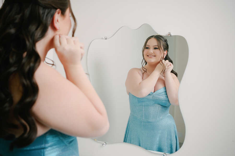 O reflexo da ansiedade boa! A debutante coloca os últimos detalhes, um brinco, admirando-se no espelho. Fotografia de making of em Jacareí, capturando a preparação para a grande noite no Espaço Lisbon.