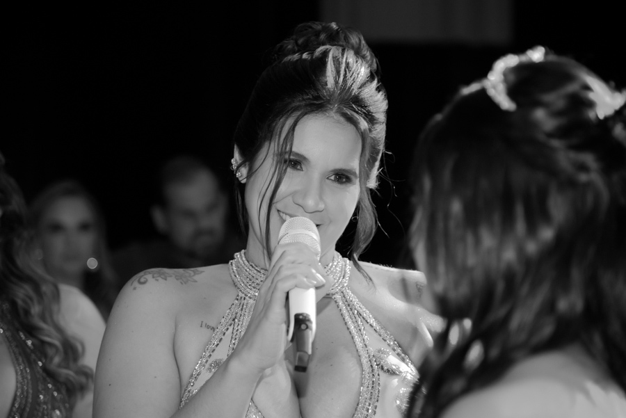 Close em preto e branco de uma convidada emocionada discursando ao microfone para a debutante Juju Salini no Espaço Le Six, em Jacareí. O registro captura um momento de carinho e homenagem durante o protocolo da festa de 15 anos.