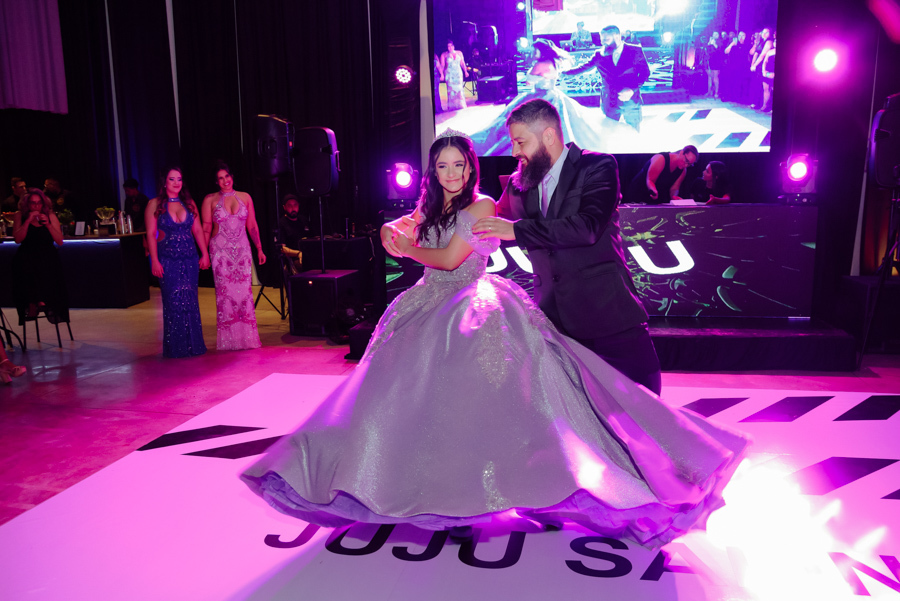 Momento da valsa de 15 anos de Juju Salini com seu pai no Espaço Le Six, em Jacareí. O registro captura a sintonia do passo de dança na pista personalizada, destacando o movimento do vestido de gala lilás sob a iluminação vibrante do salão.