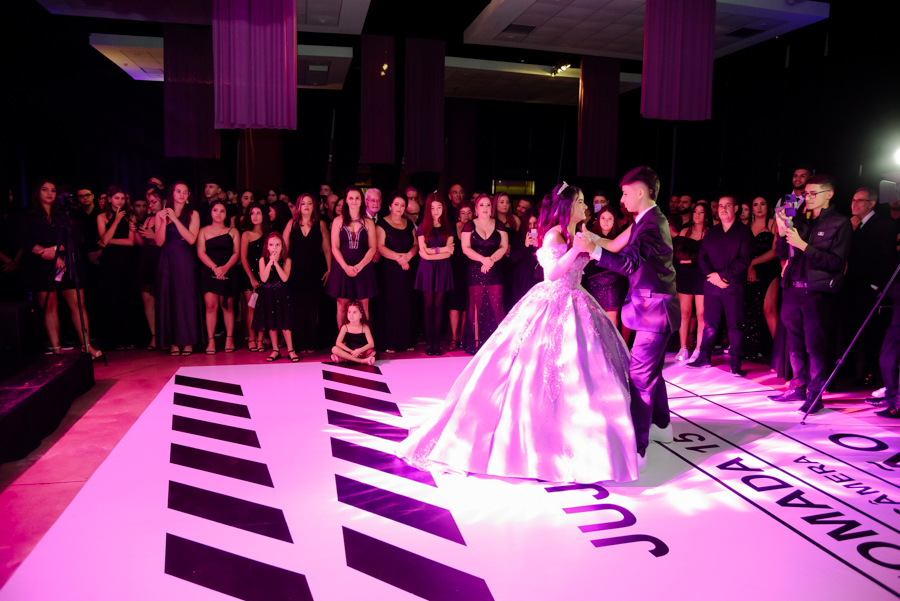 Momento da valsa de 15 anos entre a debutante Juju Salini e seu príncipe na pista personalizada do Espaço Le Six, em Jacareí. A cena, sob iluminação rosa vibrante, destaca o brilho do vestido de gala e a atenção dos convidados ao redor do salão.