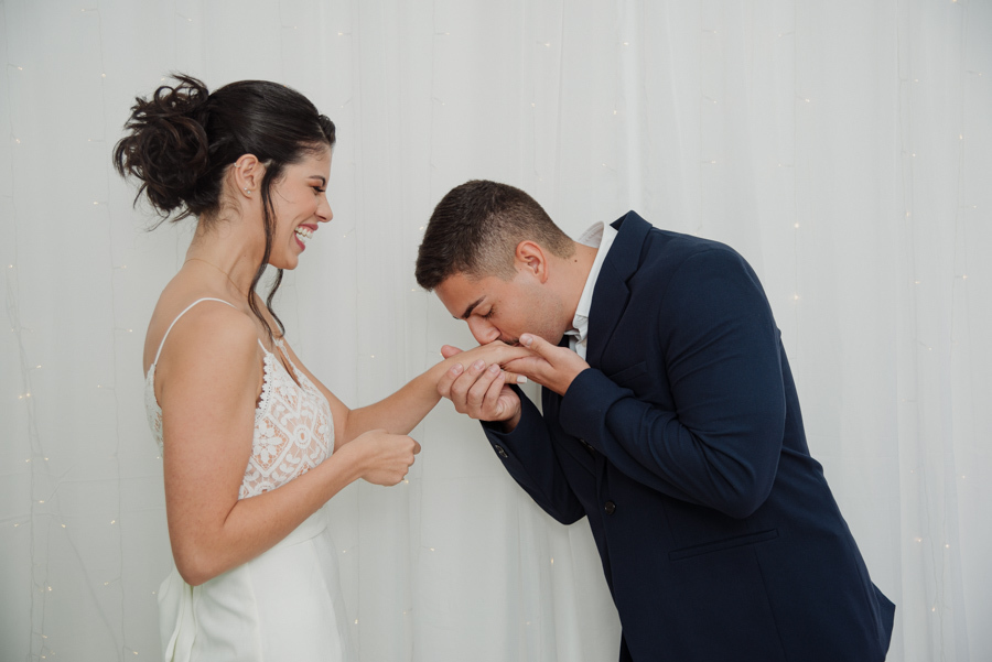 Noivo Diego beija a mão da noiva Karla após a troca de alianças em casamento civil no Cartório de Jacareí. Fotografia de casamento emocionante capturando o carinho e a felicidade dos noivos durante a cerimônia oficial na região de SJC.