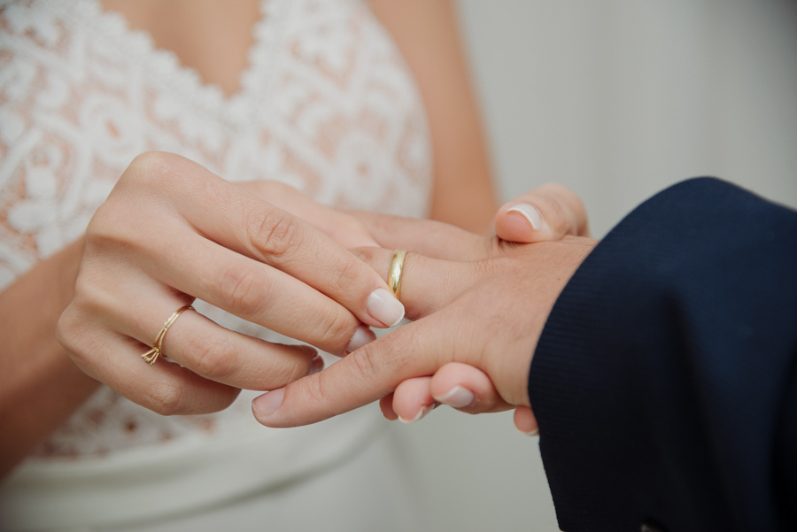 Close de fotógrafo de casamento em Jacareí mostrando a noiva colocando a aliança de ouro no dedo do noivo. Fotografia de detalhes em casamento civil, destacando o simbolismo da união e a delicadeza do momento no Cartório de Jacareí.