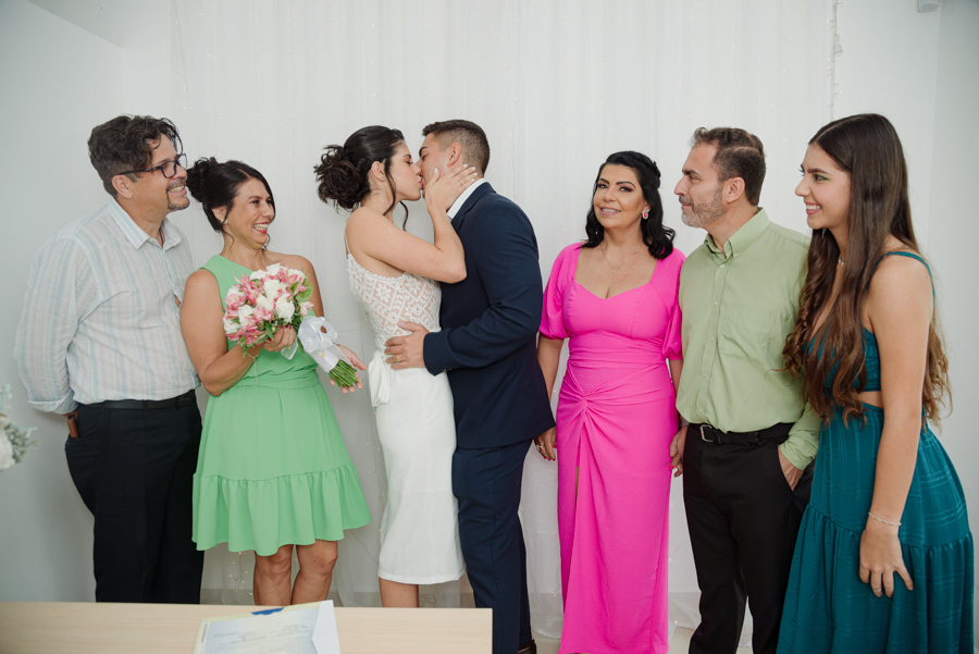 Beijo dos noivos Karla e Diego comemorando a união oficial no Cartório de Jacareí ao lado de seus familiares. Fotografia de casamento civil que captura a alegria e a celebração após o 