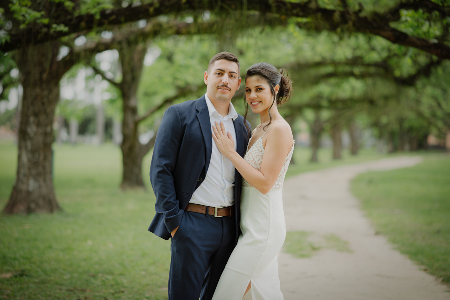 Noivos Karla e Diego posam para fotógrafo de casamento em São José dos Campos sob as árvores do Parque da Cidade. Retrato clássico e elegante do casal após o casamento civil, destacando a beleza do cenário natural e a harmonia dos recém-casados.