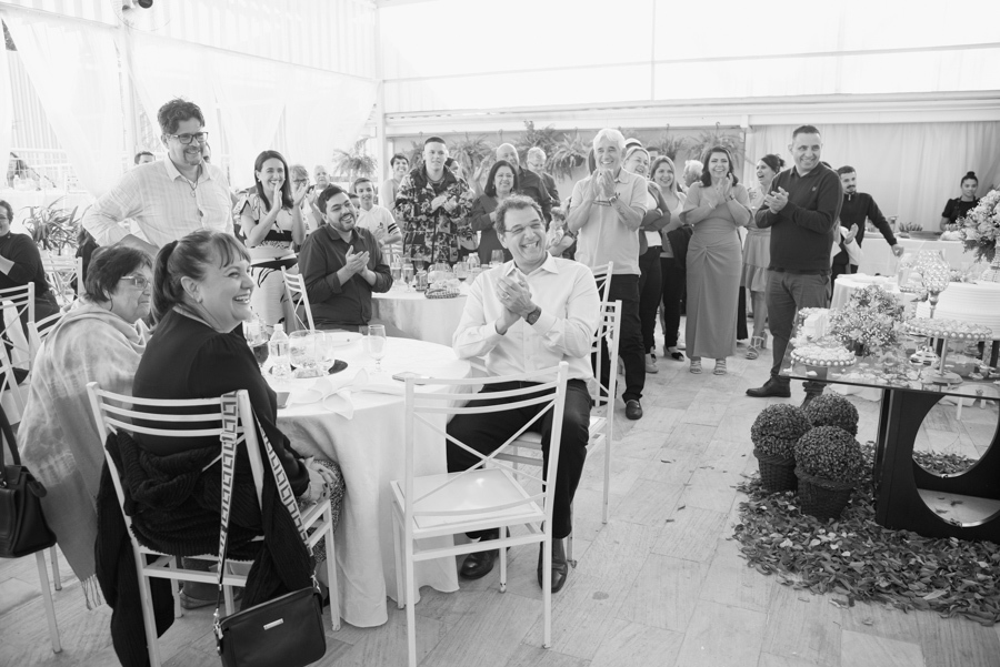 Foto preto e branco de convidados sorrindo e aplaudindo durante recepção de casamento em Jacareí. Fotógrafo de casamento captura a alegria dos amigos e familiares em celebração festiva após cerimônia civil de Karla e Diego no Vale do Paraíba.