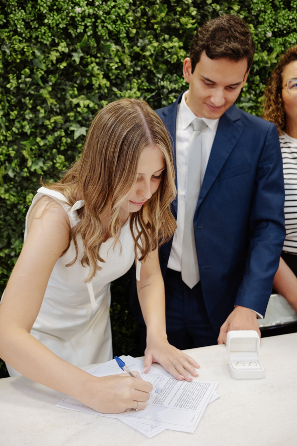 Noiva assina documentos do casamento civil no Cartório de São José dos Campos, com o noivo ao lado sorrindo. Fotografia de casamento civil em SJC destacando a união de Ana Luiza e Felipe Antônio em um momento de felicidade e cumplicidade.