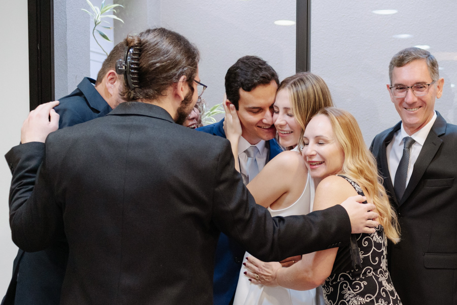 Abraço coletivo entre Ana Luiza, Felipe Antônio e seus familiares após a cerimônia de casamento civil em São José dos Campos. Fotografia de casamento civil em SJC que registra o carinho, a união familiar e a emoção deste momento especial.