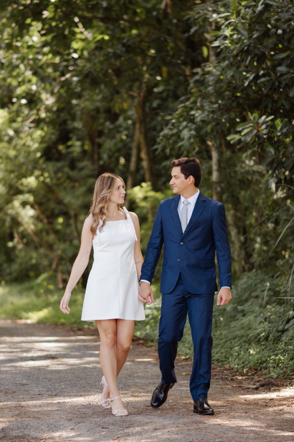 Casal de noivos caminha de mãos dadas por uma trilha arborizada no Parque da Cidade em São José dos Campos. Fotografia de casamento civil em SJC que captura a leveza e o romance de Ana Luiza e Felipe Antônio durante ensaio no Parque Roberto Burle Marx.
