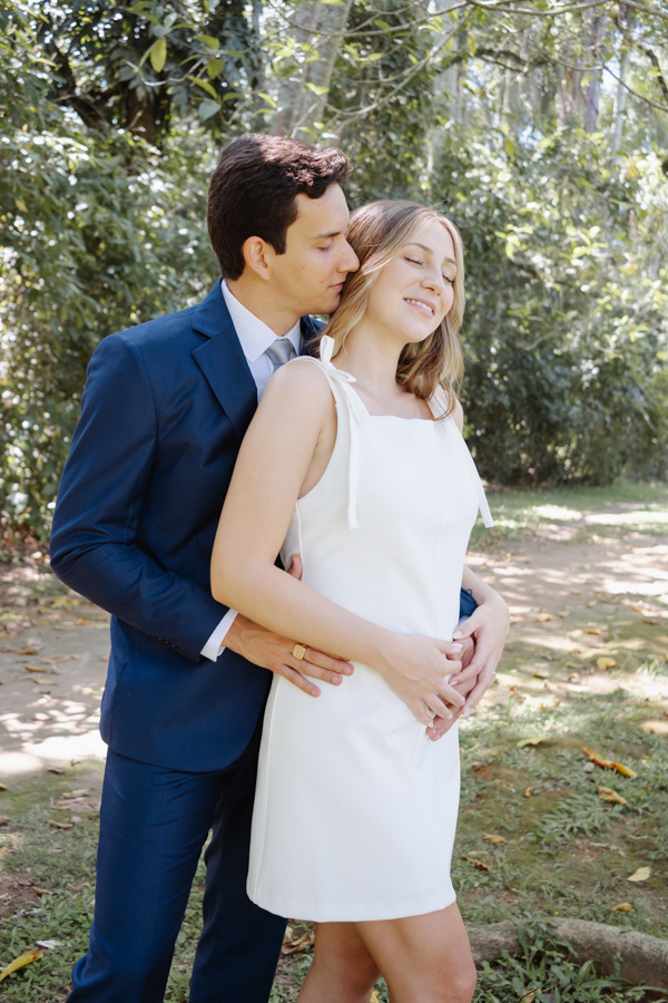 Noivo abraça a noiva grávida por trás, mantendo as mãos sobre sua barriga durante ensaio no Parque da Cidade em São José dos Campos. Fotografia de casamento civil em SJC que transmite a ternura e a expectativa de Ana Luiza e Felipe Antônio pela Laura.