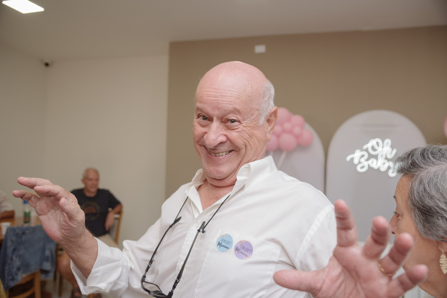 Familiar sorridente vibra durante o chá revelação de Diego e Tamires. Ele usa camisa branca com adesivos 