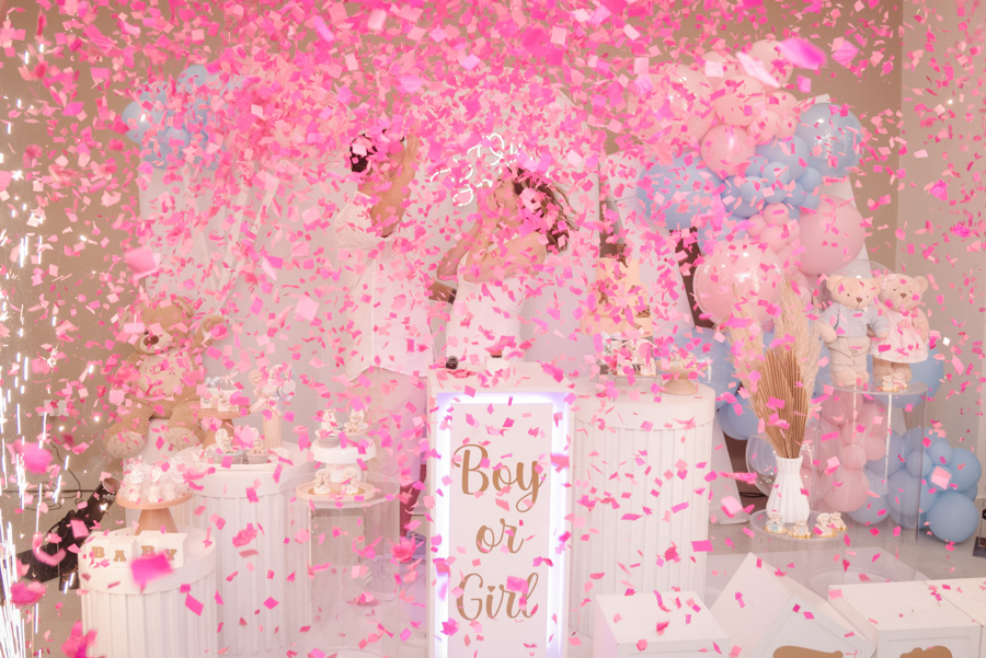 Uma densa chuva de papéis rosa cobre Diego e Tamires no momento da grande revelação. A imagem transborda a emoção descrita no texto, com a vida do casal se tingindo de rosa sob os aplausos e a alegria contagiante de todos os presentes no chá revelação.