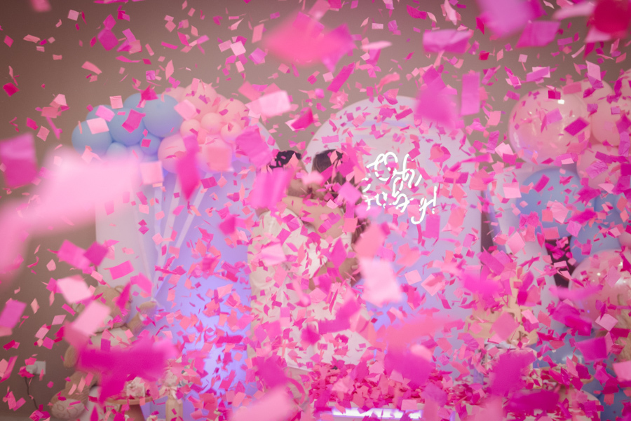 Close-up do casal Diego e Tamires se abraçando e celebrando em meio a uma densa e mágica chuva de papéis rosa. O momento marca a revelação de que a vida da nova família se tingiu de rosa, transbordando a emoção e alegria registradas no chá revelação.