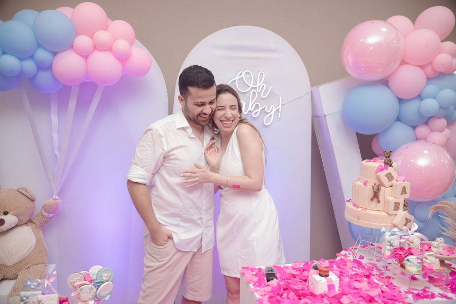 Diego e Tamires sorriem e celebram com cumplicidade após a grande revelação. O cenário está repleto de papéis rosa, simbolizando que a vida da família se tingiu de rosa, em um momento de pura alegria e descontração registrado neste capítulo especial.