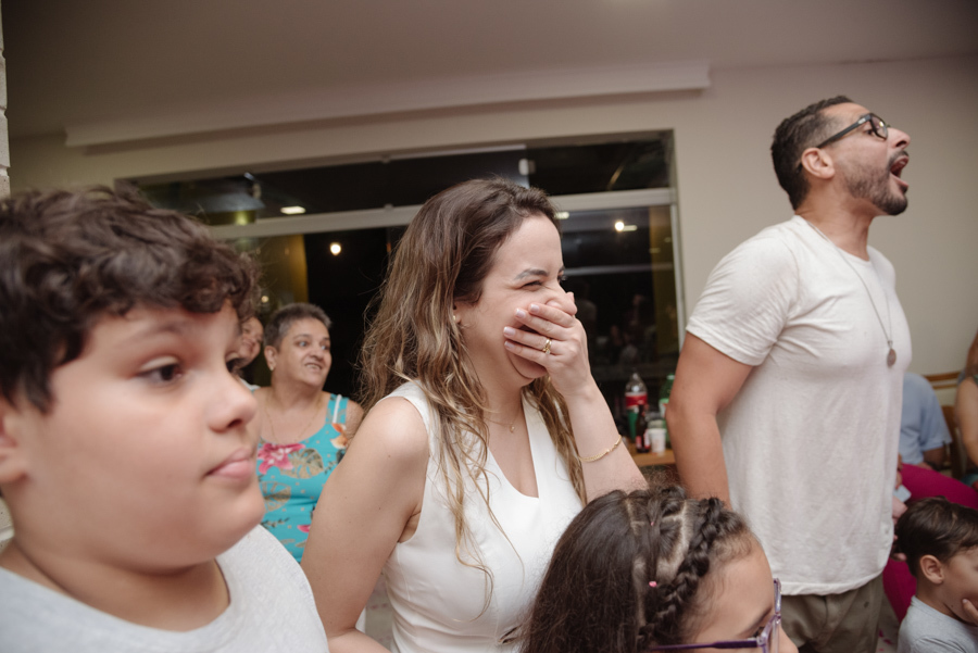 Tamires ri e cobre o rosto com a mão em um momento de pura diversão após a revelação. O chão coberto de papéis rosa confirma que a vida da nova família se tingiu de rosa, enquanto Diego e os convidados celebram com entusiasmo ao seu redor.