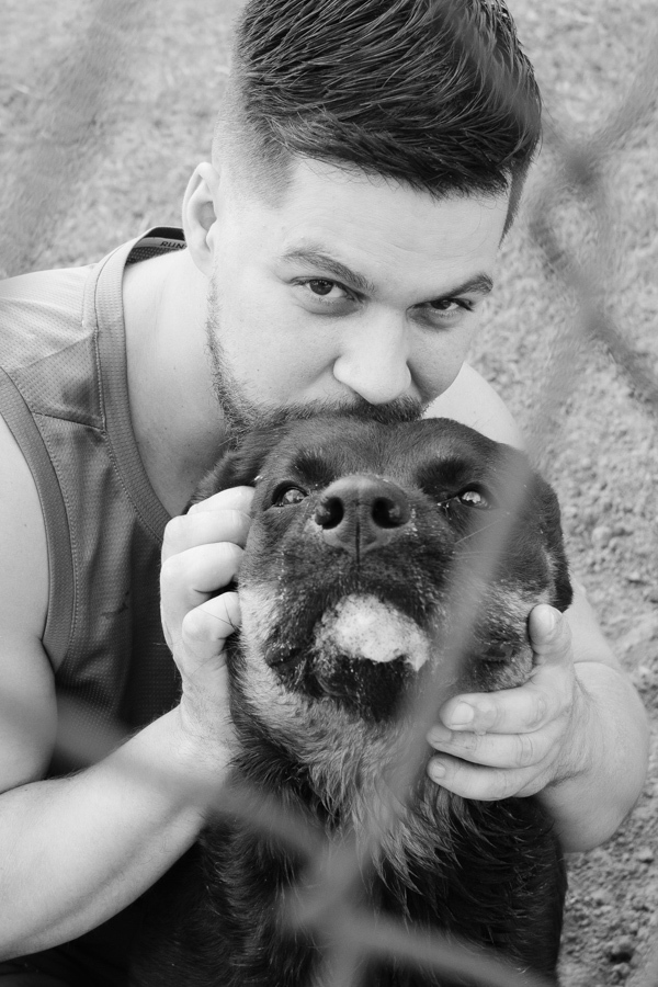 Fotografia de casamento em Jacareí: momento afetivo do noivo Matthaus com seu cachorro de estimação. Foto em preto e branco com foco no beijo carinhoso e na expressão de lealdade do pet, destacando a sensibilidade e os laços familiares do casal.