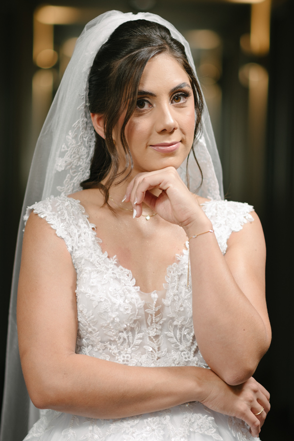 Fotografia de casamento em Jacareí: retrato clássico da noiva Rebeca no Ibis Hotel. Close-up elegante destacando o véu, o vestido rendado e a maquiagem impecável, com pose suave e olhar sereno capturados após o making of para a Chácara Lopes.