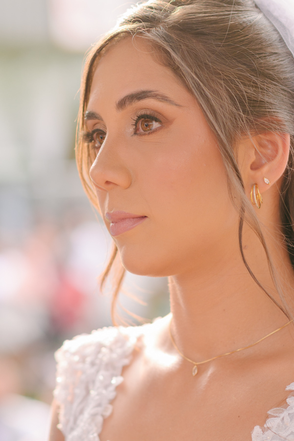 Fotografia de casamento em Jacareí: close da noiva Rebeca no altar da Chácara Lopes. Perfil detalhado sob a luz suave do entardecer, destacando a maquiagem delicada, os brincos dourados e o olhar emocionado durante a cerimônia ao ar livre.