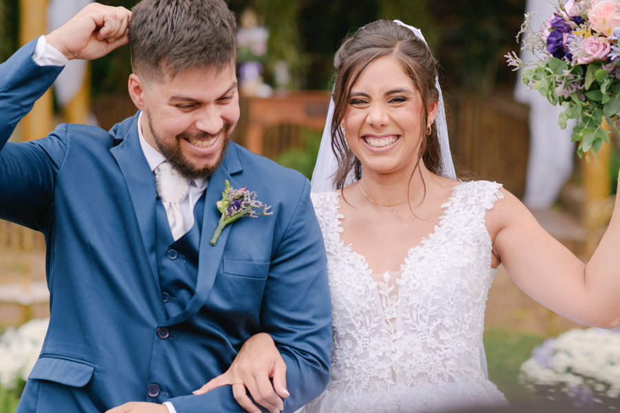 Fotografia de casamento em Jacareí: saída vibrante de Matthaus e Rebeca na Chácara Lopes. Os noivos sorriem e celebram com euforia após o sim, com a noiva erguendo o buquê em um momento de pura felicidade sob a luz natural do entardecer.