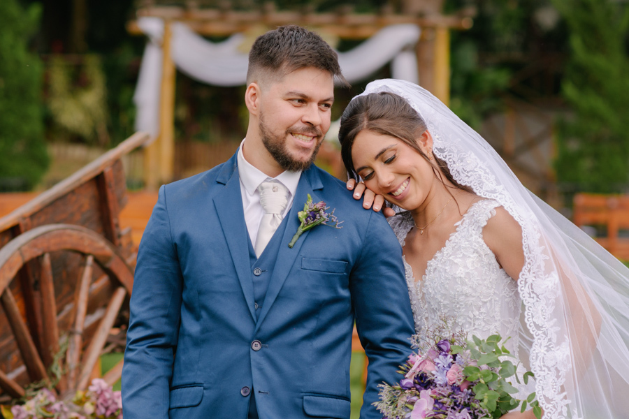 Fotografia de casamento em Jacareí: retrato romântico de Matthaus e Rebeca na Chácara Lopes. A noiva encosta o rosto no ombro do noivo, ambos sorrindo sob a luz do entardecer, com o altar rústico e uma carruagem de madeira ao fundo.