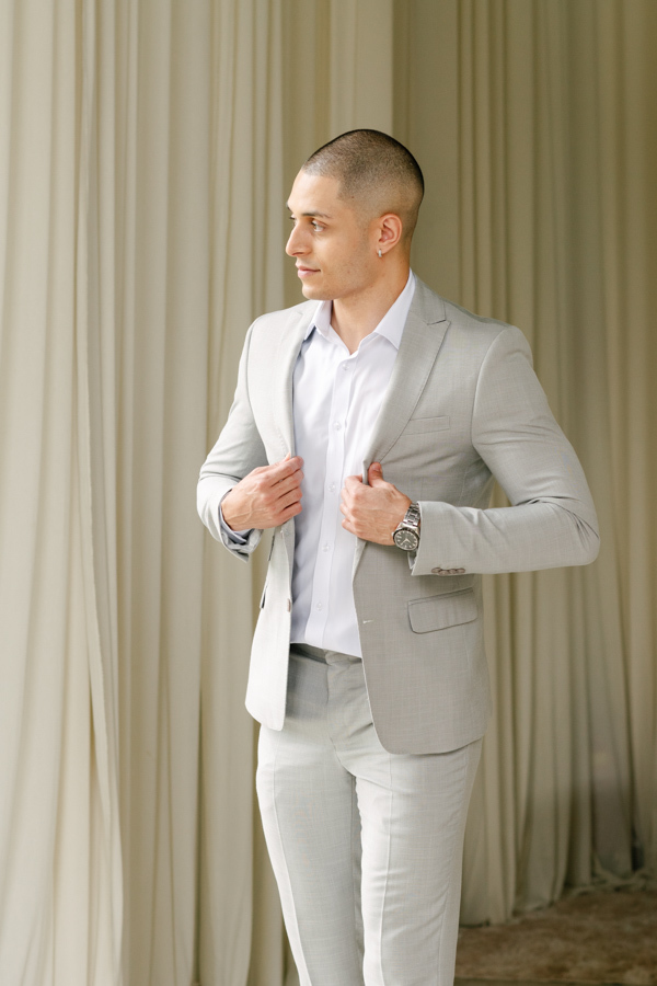 Noivo Luidgi ajustando o paletó cinza durante o making of na Chácara Mariah. Fotografia de casamento em Jacareí capturando a elegância e os detalhes da preparação do noivo. Registro profissional realizado por fotógrafo de casamento em Jacareí.