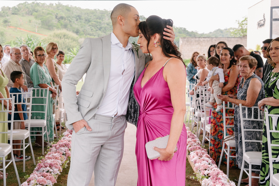 Noivo Luidgi beijando a testa de sua mãe no altar durante cerimônia ao ar livre na Chácara Mariah. Fotografia de casamento em Jacareí capturando momento de carinho e emoção. Registro profissional por fotógrafo de casamento em Jacareí.