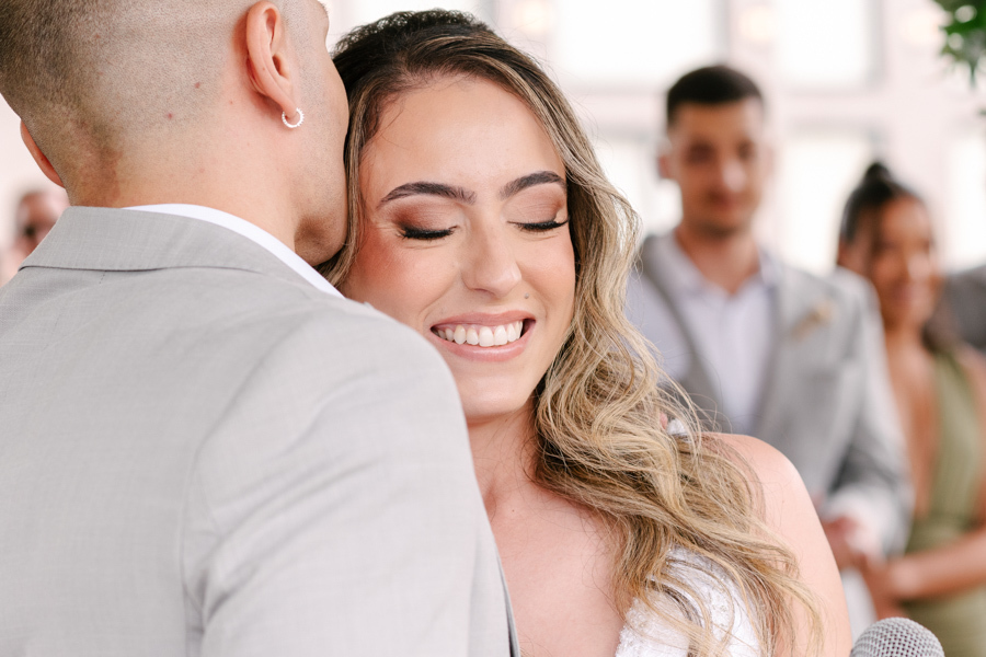 Noiva Aline sorrindo de olhos fechados enquanto recebe um carinho do noivo Luidgi no altar da Chácara Mariah, em Jacareí. Fotografia de casamento capturando afeto e felicidade. Registro profissional por fotógrafo de casamento em Jacareí.