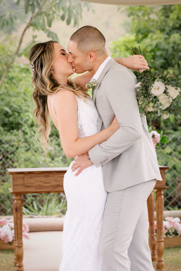 Noivos Aline e Luidgi se beijam apaixonadamente no altar da Chácara Mariah, em Jacareí. Fotografia de casamento ao ar livre capturando romantismo e felicidade após a cerimônia. Registro profissional realizado por fotógrafo de casamento em Jacareí.