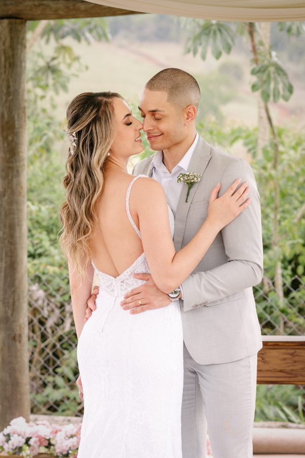 Noivos Aline e Luidgi abraçados no altar da Chácara Mariah, em Jacareí, com os rostos próximos em momento romântico. Fotografia de casamento destacando o decote nas costas do vestido da noiva e o carinho do casal. Registro por fotógrafo em Jacareí.