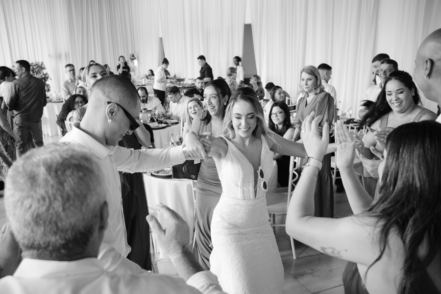 Noivos Aline e Luidgi dançam animados cercados por convidados durante a festa na Chácara Mariah, em Jacareí. Fotografia de casamento em preto e branco capturando a energia da pista de dança. Registro profissional por fotógrafo de casamento em Jacareí.