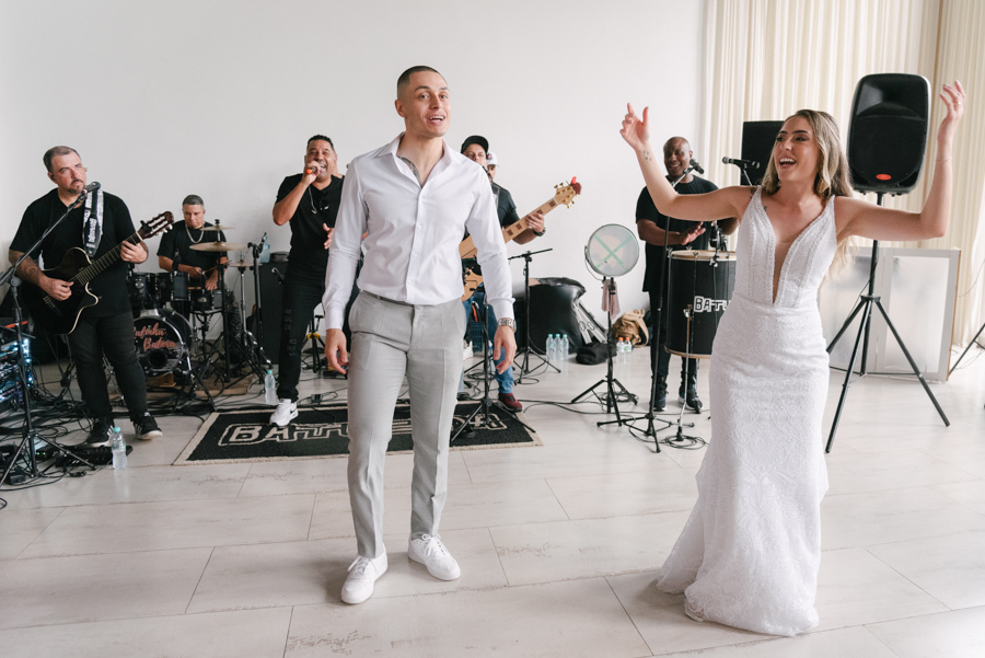 Noivos Aline e Luidgi se divertem na pista de dança com a Banda Batucada ao fundo na Chácara Mariah, em Jacareí. Fotografia de casamento capturando a energia do show ao vivo e a alegria dos recém-casados. Registro por fotógrafo de casamento em Jacareí.
