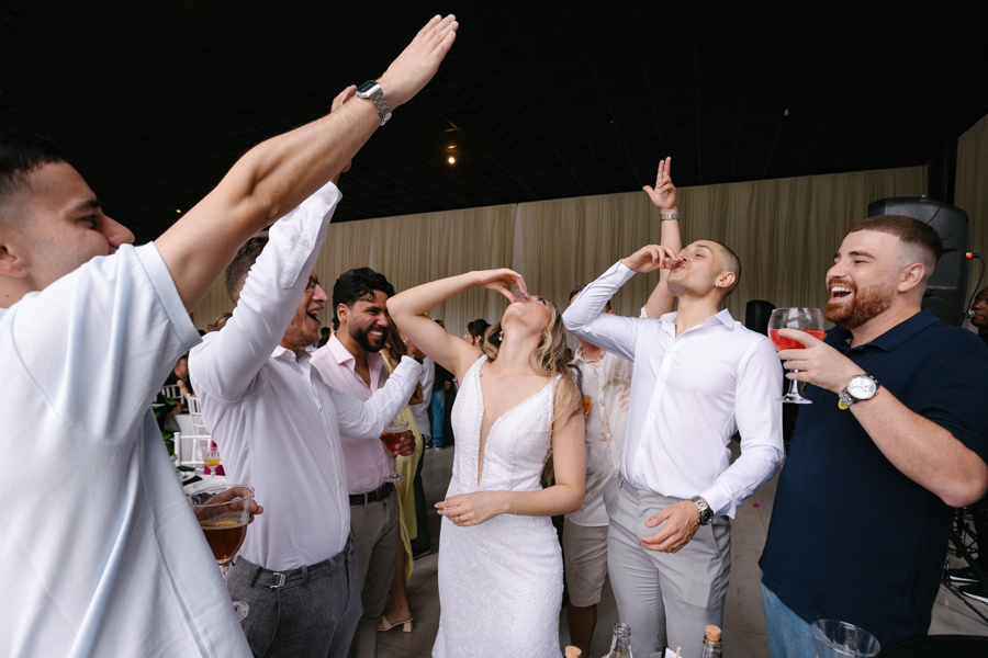 Noiva Aline e noivo Luidgi virando shots de bebida com amigos na pista de dança da Chácara Mariah, em Jacareí. Fotografia de casamento capturando a diversão e a celebração intensa da festa. Registro profissional realizado por fotógrafo em Jacareí.