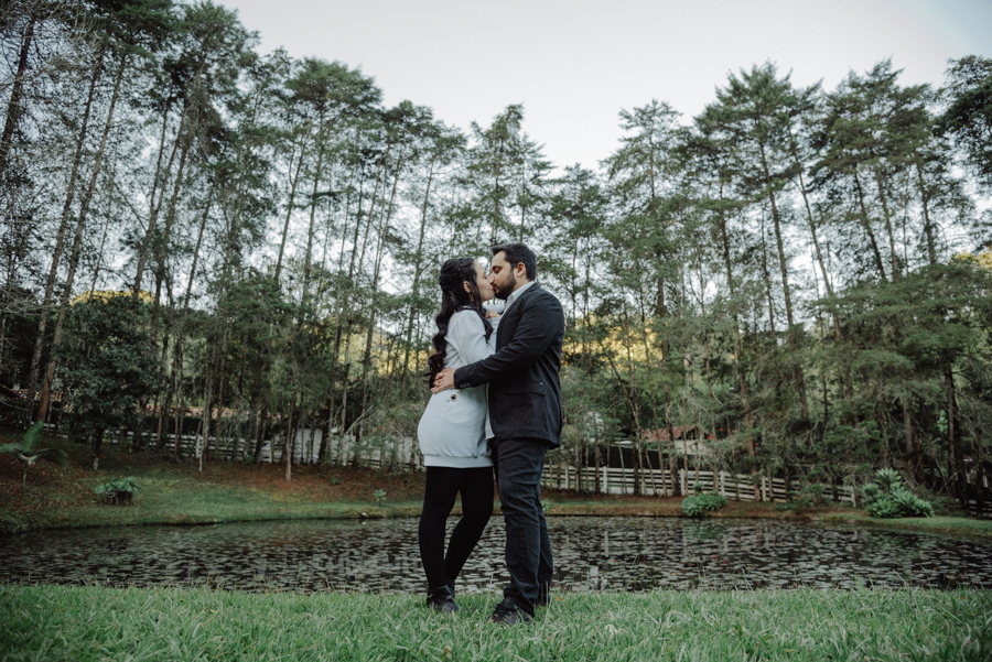 Beijo de André e Nathália em cenário de tirar o fôlego: pré-wedding em Campos do Jordão. Composição em plano aberto destacando a natureza exuberante e os pinheiros da Serra da Mantiqueira. Fotografia de casamento autêntica e cinematográfica.