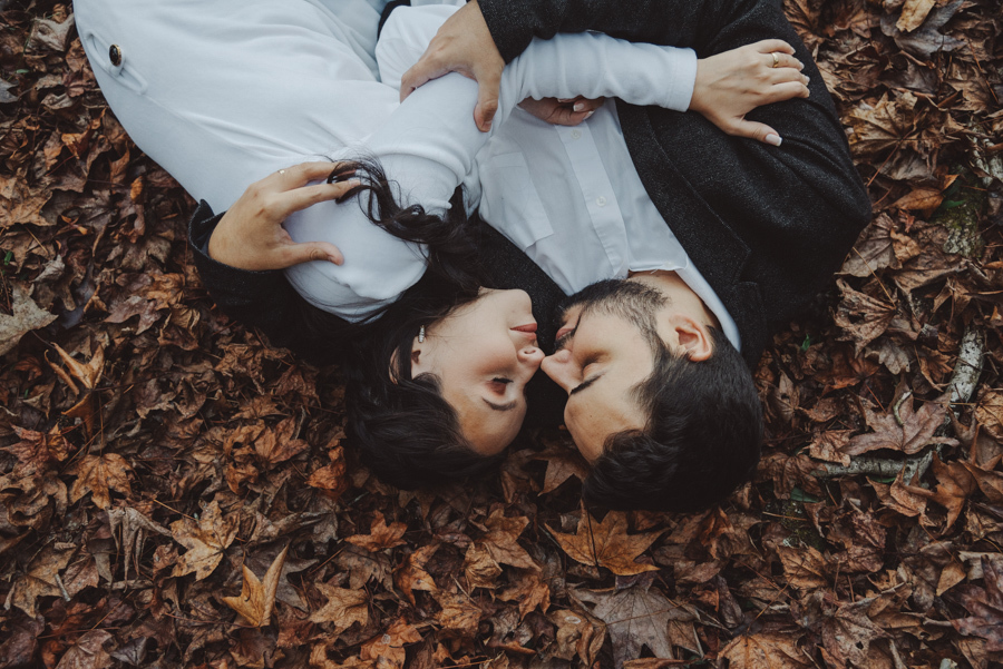 André e Nathália deitados em um tapete de folhas secas: o auge do outono em Campos do Jordão. Ensaio pré-wedding lifestyle com perspectiva superior, destacando a entrega e o romantismo do casal na Serra da Mantiqueira. Foto artística e sensível.