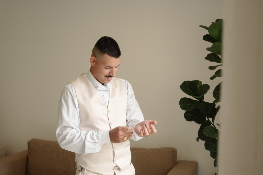 Noivo Ricardo durante o making of em Jacareí, vestindo colete bege e ajustando as abotoaduras da camisa branca. Fotografia de casamento profissional capturando os detalhes e a preparação do noivo antes da cerimônia na Chácara Mariah.
