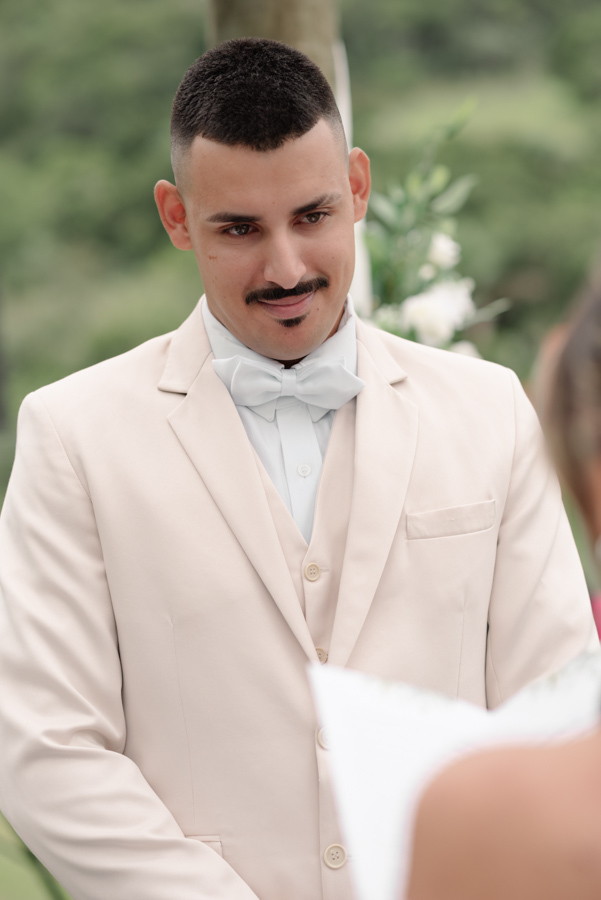 Noivo Ricardo no altar em Jacareí, visivelmente emocionado ao ouvir os votos durante a cerimônia na Chácara Mariah. Fotografia de casamento profissional capturando o olhar atento e a sensibilidade do noivo em um dos momentos mais marcantes do evento.