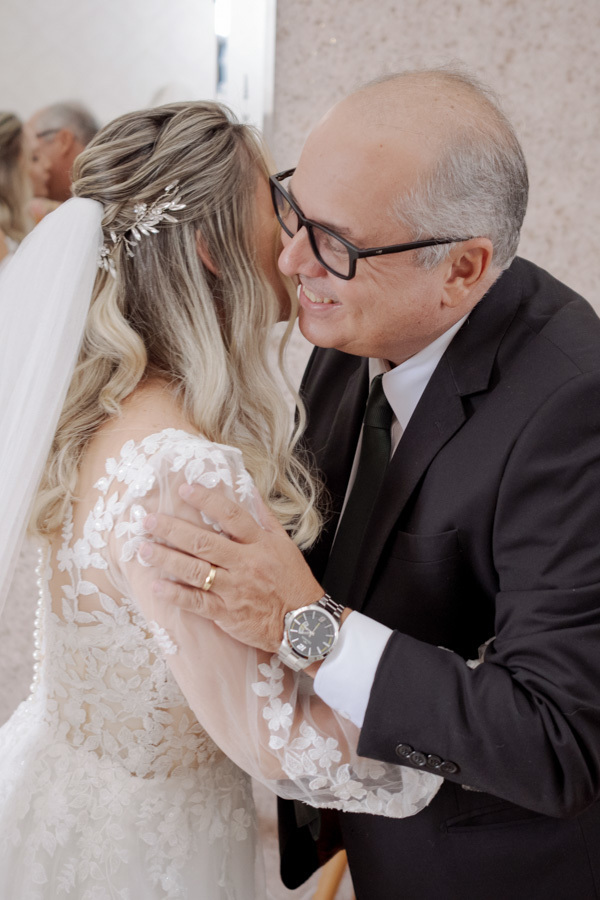 Noiva Claudia recebe abraço carinhoso do pai durante o making of em Jacareí. Momento de profunda emoção e cumplicidade antes da cerimônia, registrado com sensibilidade pelo fotógrafo de casamentos Gilson Dias.