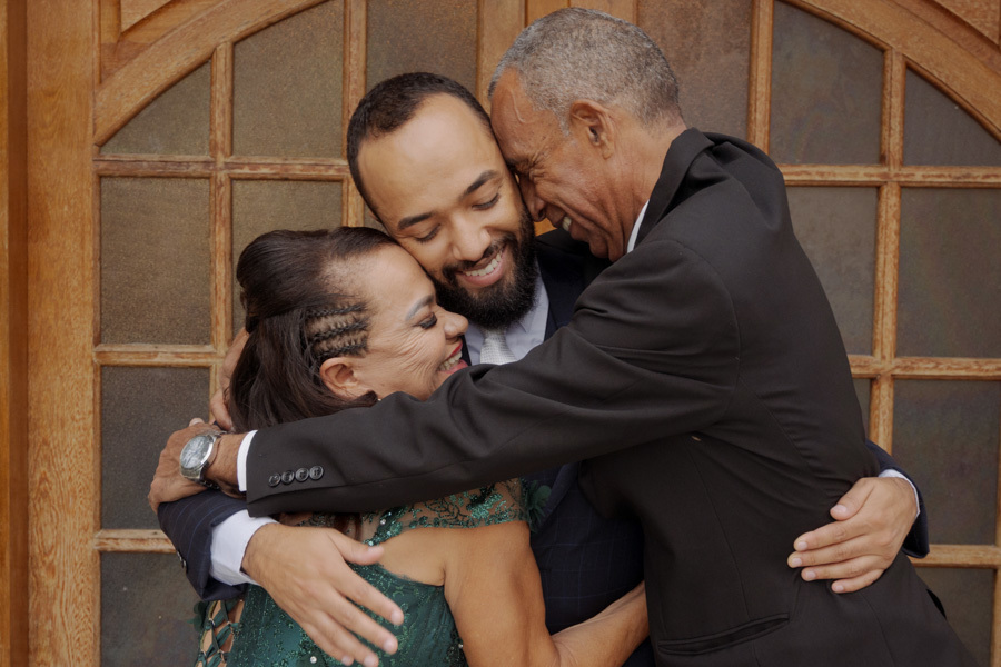 Abraço emocionante entre o noivo Matheus e seus pais durante o making of em Jacareí. Fotografia de casamento que captura a gratidão e o amor familiar em um momento espontâneo e verdadeiro, registrada pelo fotógrafo Gilson Dias.